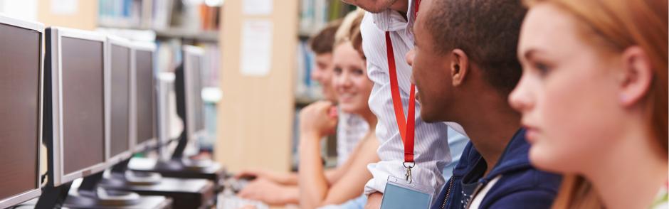 Students Working At Computers In Library With Teacher