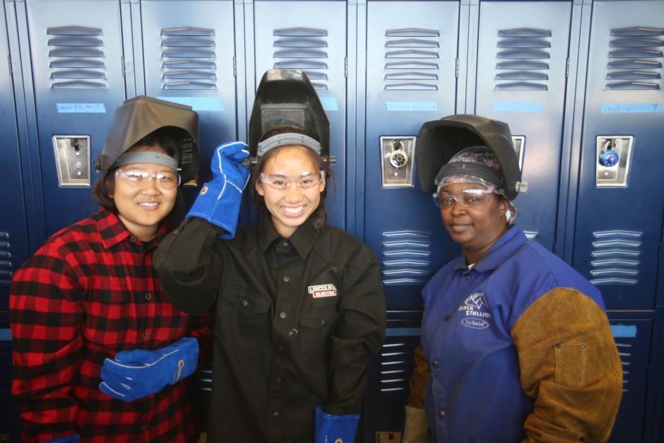 A female LBCC wleding student standing with two female high school students.