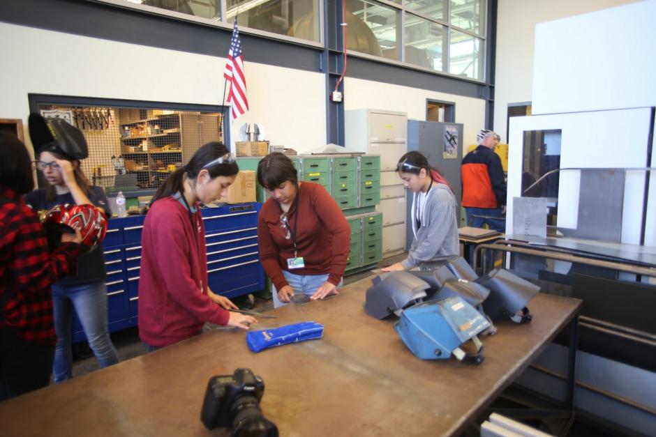 A group of female high school students filing down sheet metal.