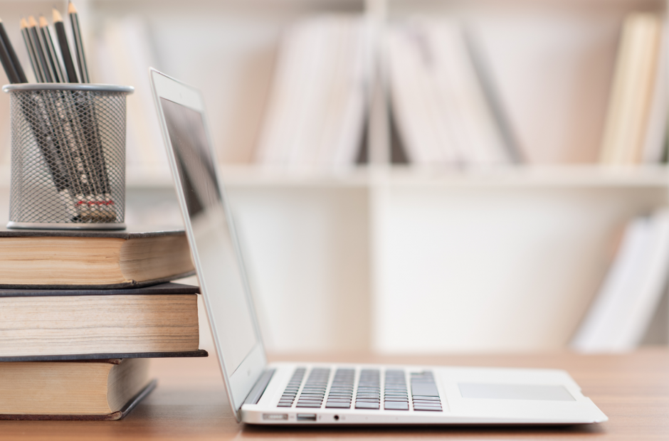 Laptop with books on desk. Cup of pencils. 