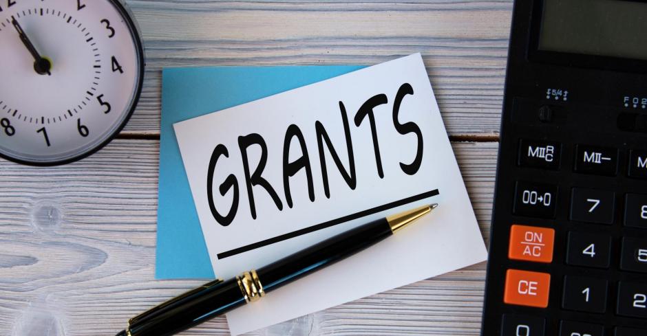 GRANTS - word on a white sheet on the background of a calculator, alarm clock and pen. Business concept