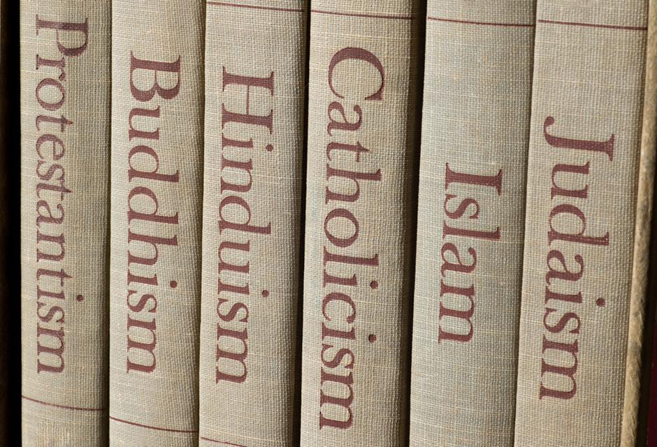 Book spines listing major world religions - Judaism, Islam, Catholicism, Hinduism, Buddhism and Protestantism.