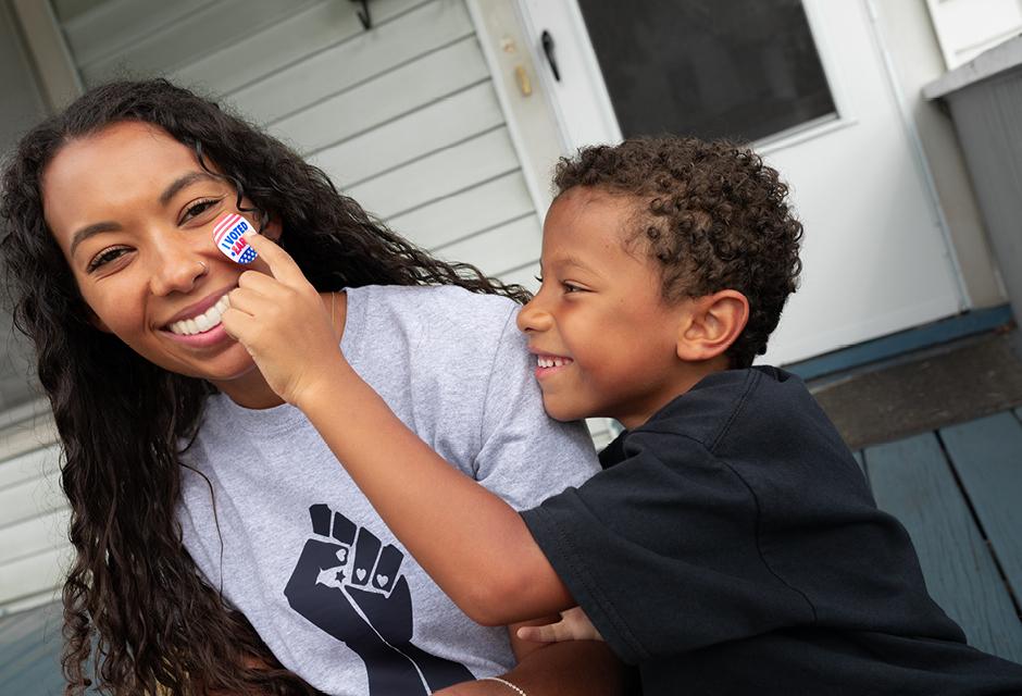 African American son placing I Voted Early Sticker on smiling black mother's face 