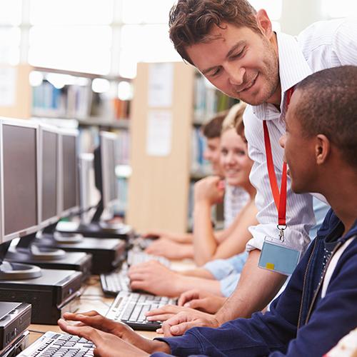 Students Working At Computers In Library With Teacher